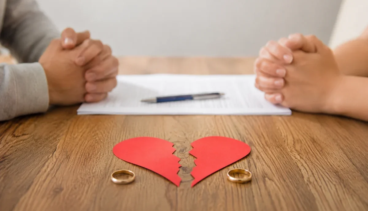Filing for divorce in Texas: a torn red paper heart and separated wedding rings on a wooden table between a man and woman.